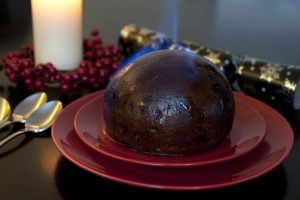 Flaming traditional fruity Christmas pudding set alight with brandy before serving on a festive Xmas table for dinner